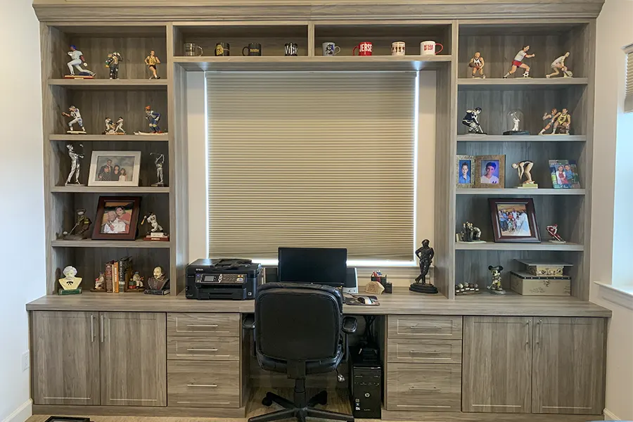 Custom home office featuring a built-in desk, gray wood-grain finish, open display shelving, storage cabinets, drawers, and integrated workspace organization by Custom Closets A&G Designs.