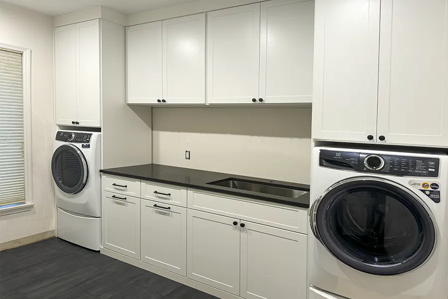 Custom laundry room with floor-to-ceiling storage cabinets, countertop workspace, utility sink, and built-in laundry organization system.