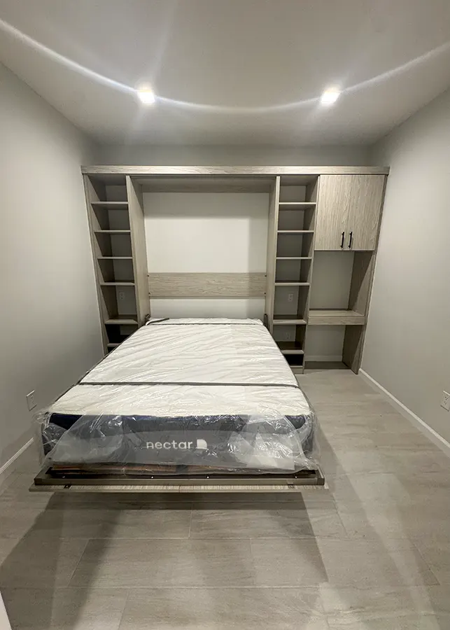 Custom Murphy bed in open position featuring Tafisa Weekend Gateway finish, built-in shelving, upper storage cabinets, integrated desk workspace, and space-saving guest room design by Custom Closets A&G Designs.
