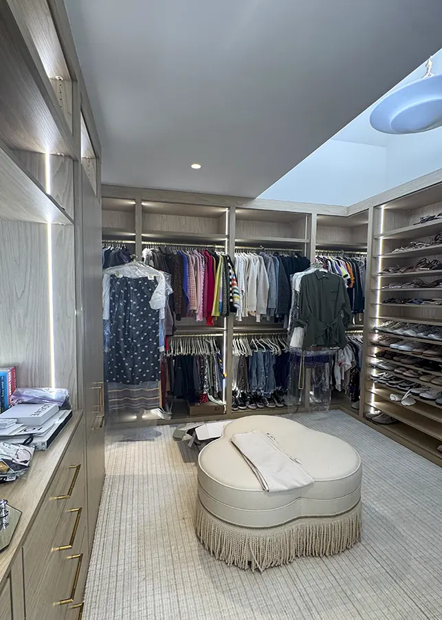 Walk-in closet with LED shelving, shoe storage, hanging sections, and central seating area.