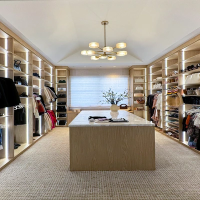 Large luxury walk-in closet with illuminated shelving, central island, and organized clothing displays