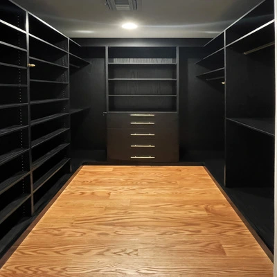 Contemporary walk‑in closet with dark custom cabinetry, open shelving, hanging space, and a central drawer unit in a Long Island